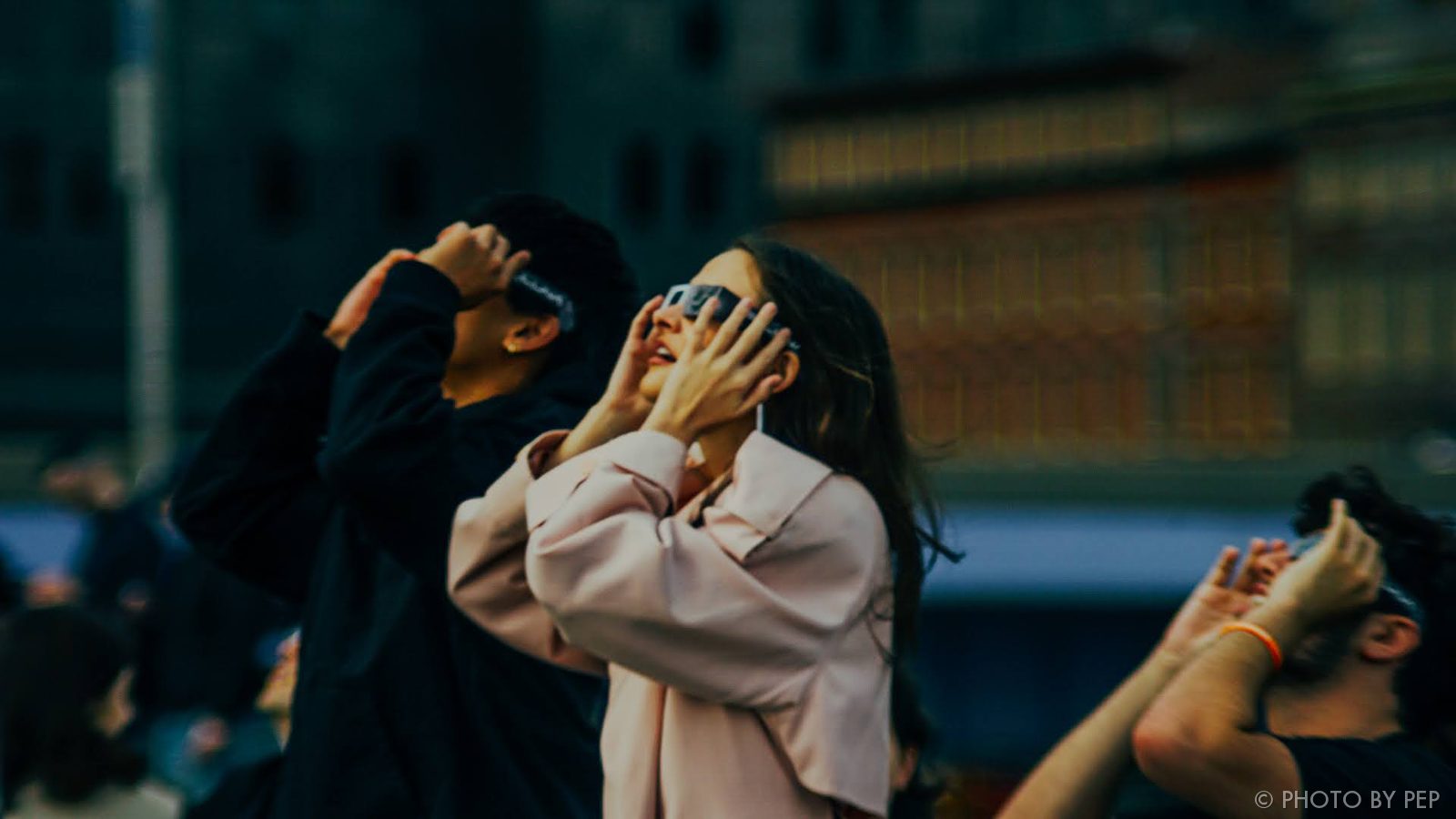 People looking up through solar eclipse glasses in the city
