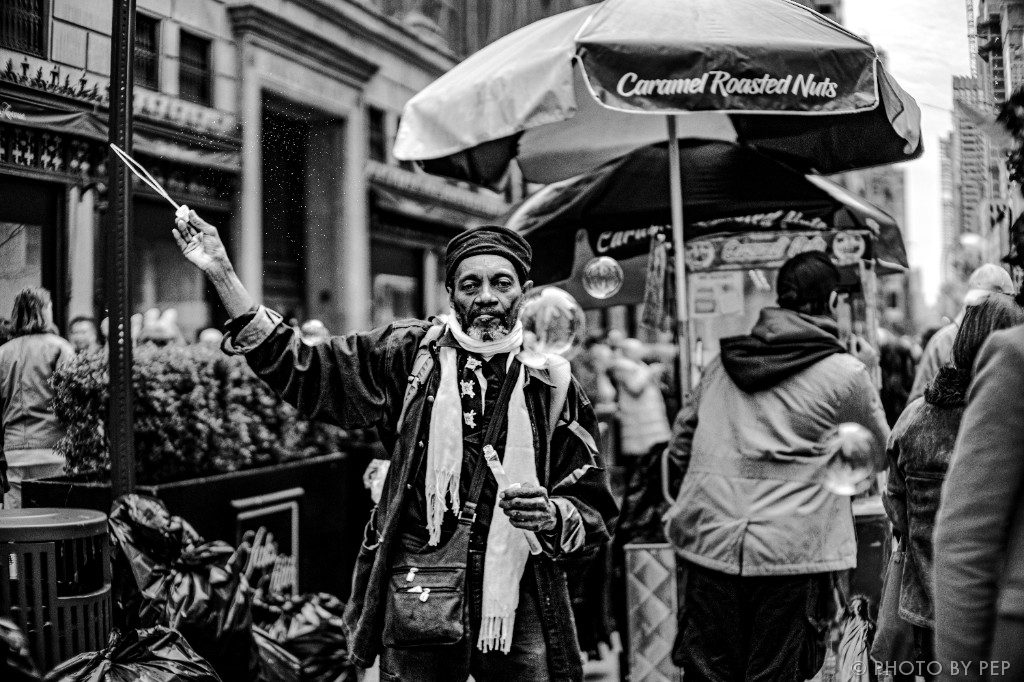 Black-and-white street portrait of a man with bubble wands on a New York sidewalk